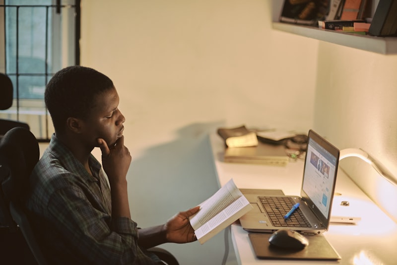Un étudiant à sa table de travail, un document à la main, prépare son dossier de candidature devant son ordinateur portable